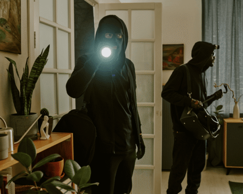 Two masked burglars breaking into a house at night, shining a flashlight, symbolizing a serious crime leading to conspiracy theft charges San Diego.