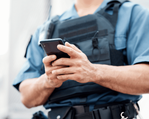 Police officer in uniform and tactical vest operating a smartphone, illustrating the legal question of a cell phone search warrant San Diego and digital privacy rights.
