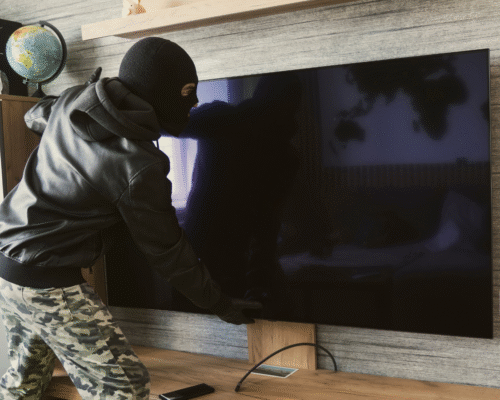 Masked person in a leather jacket and camouflage pants attempting to remove a flat-screen television, symbolizing San Diego receiving stolen property cases and legal defenses based on knowledge, item value thresholds, and California Penal Code 496 under Proposition 47.
