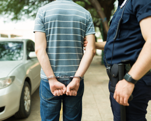 A person in handcuffs standing beside a police officer near a parked vehicle, representing a hit and run arrest and the legal consequences of leaving the scene of an accident in San Diego.