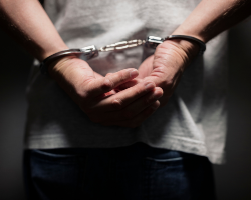 A person standing with their hands cuffed behind their back, emphasizing the seriousness of facing criminal charges and the need for a strong legal defense strategy.