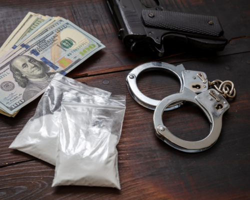 Handgun, cash, plastic bags of white powder, and handcuffs on a table, representing drug charges involving a firearm and the increased criminal penalties such cases can carry in Fallbrook, California.