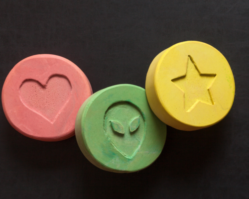 Colorful pressed tablets resembling MDMA (ecstasy) with stamped symbols, illustrating drug distribution charges and the legal risks associated with possession with intent to sell under California law.