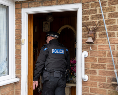 A police officer entering a private residence through an open doorway, raising important questions about consent, search authority, and Fourth Amendment rights in shared living situations.