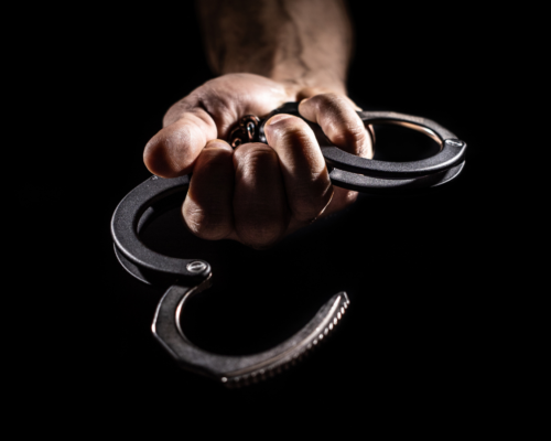 Close-up of a hand gripping metal handcuffs against a dark background, symbolizing arrest, criminal charges, and the serious consequences of domestic violence allegations.