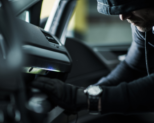 Hooded person reaching into the interior of a vehicle, representing theft charges, property crimes, and the potential immigration consequences of criminal convictions for non-citizens in California.