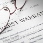 Arrest Warrant document with reading glasses