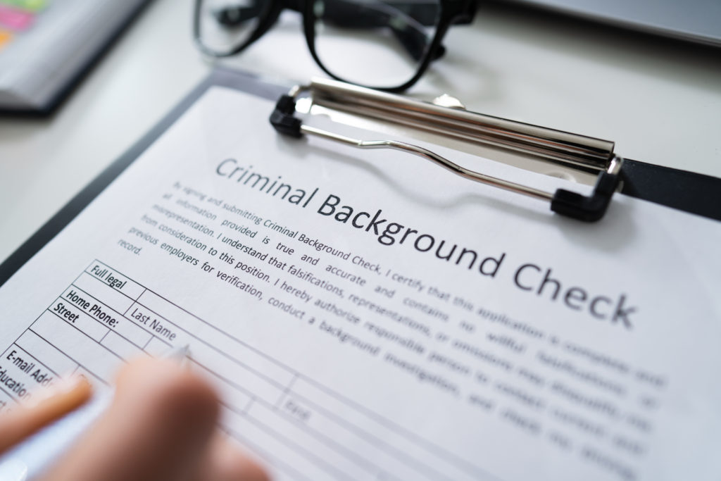 Close-up Of Human Hand Filling Criminal Background Check Application Form With Pen