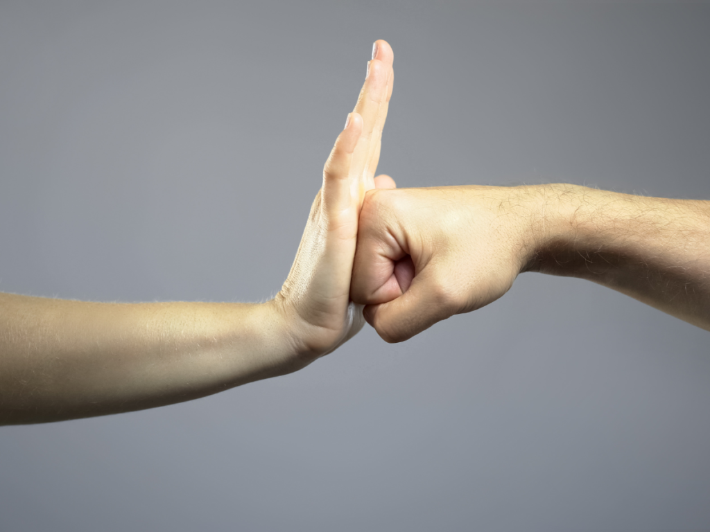 A hand blocking a punch in front of a grey background.