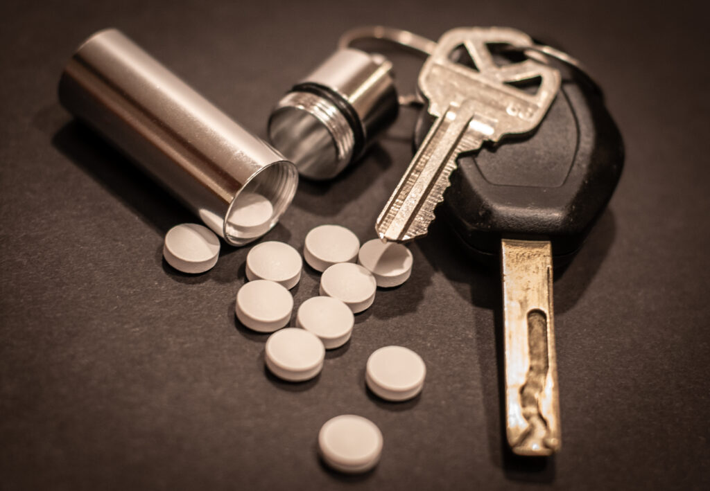 Pills are strewn out of a cylindrical container attached to a keyring.