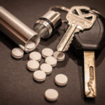 Pills are strewn out of a cylindrical container attached to a keyring.