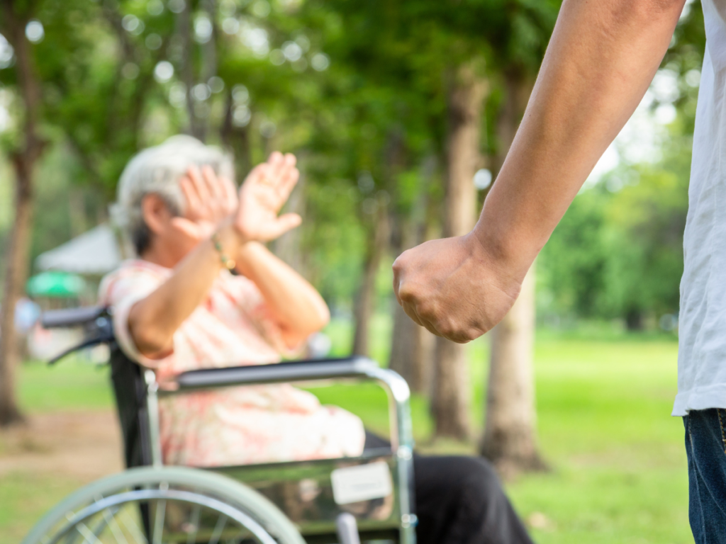 a elderly woman in a wheelchair putting both hands in front of her face. In front of her is a clenched fist.