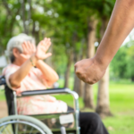 a elderly woman in a wheelchair putting both hands in front of her face. In front of her is a clenched fist.